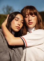 Close-up portrait of two female models with eyes closed embracing under bright natural sunlight by Silja Magg