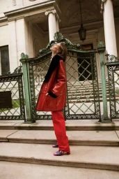 Model wearing a glossy red coat and matching red trousers standing before ornate green iron gates by photographer Silja Magg.