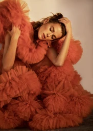 Woman in an oversized tiered terracotta tulle gown posing with arms raised in a studio