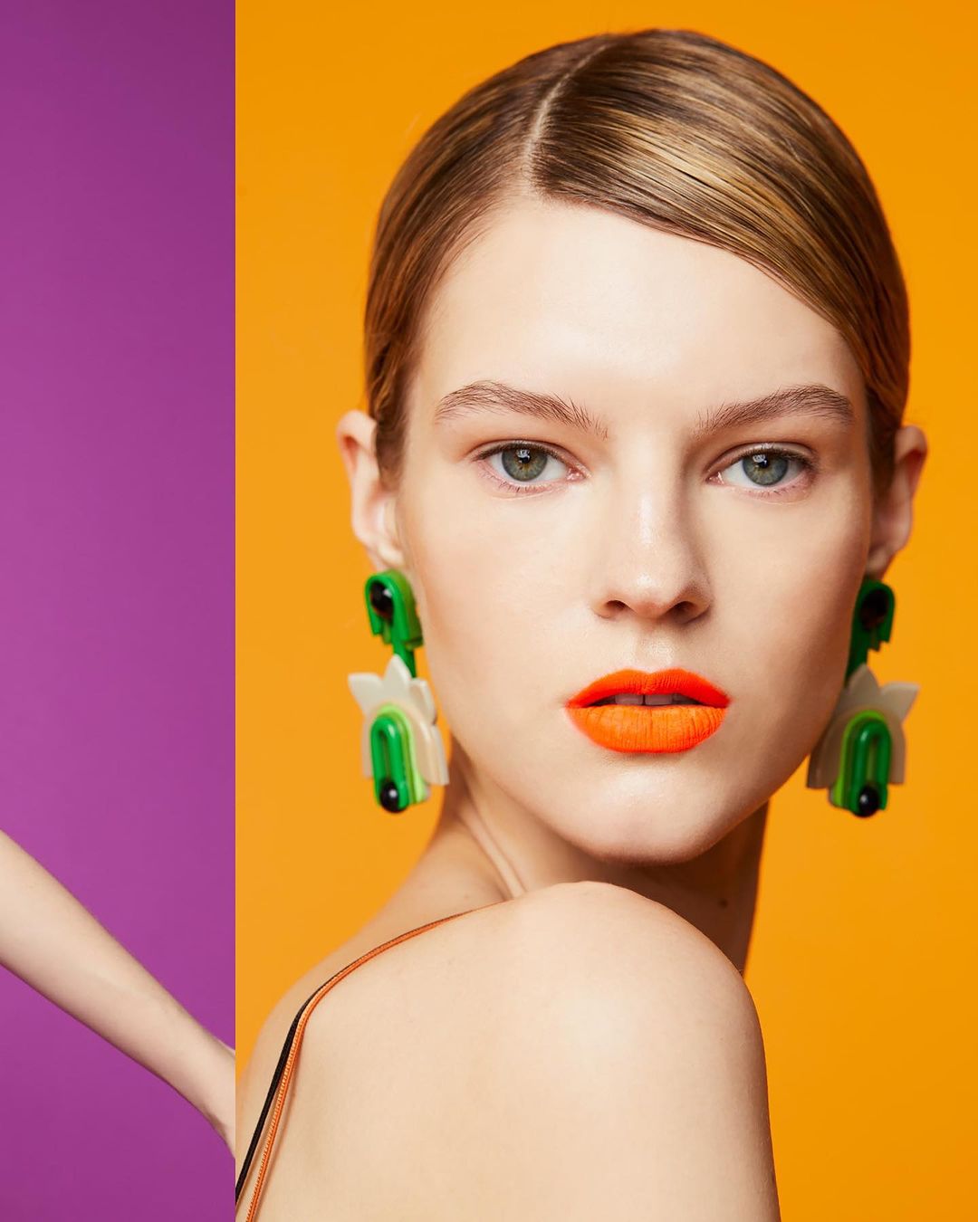 Headshot of fair-skinned model with orange lipstick and large green and white flower earrings against an orange and purple backdrop.