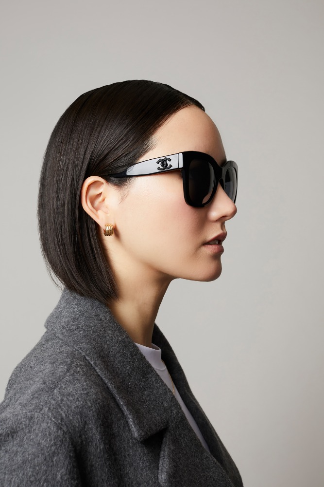 Profile portrait of a woman wearing black sunglasses and a dark grey coat against a neutral background
