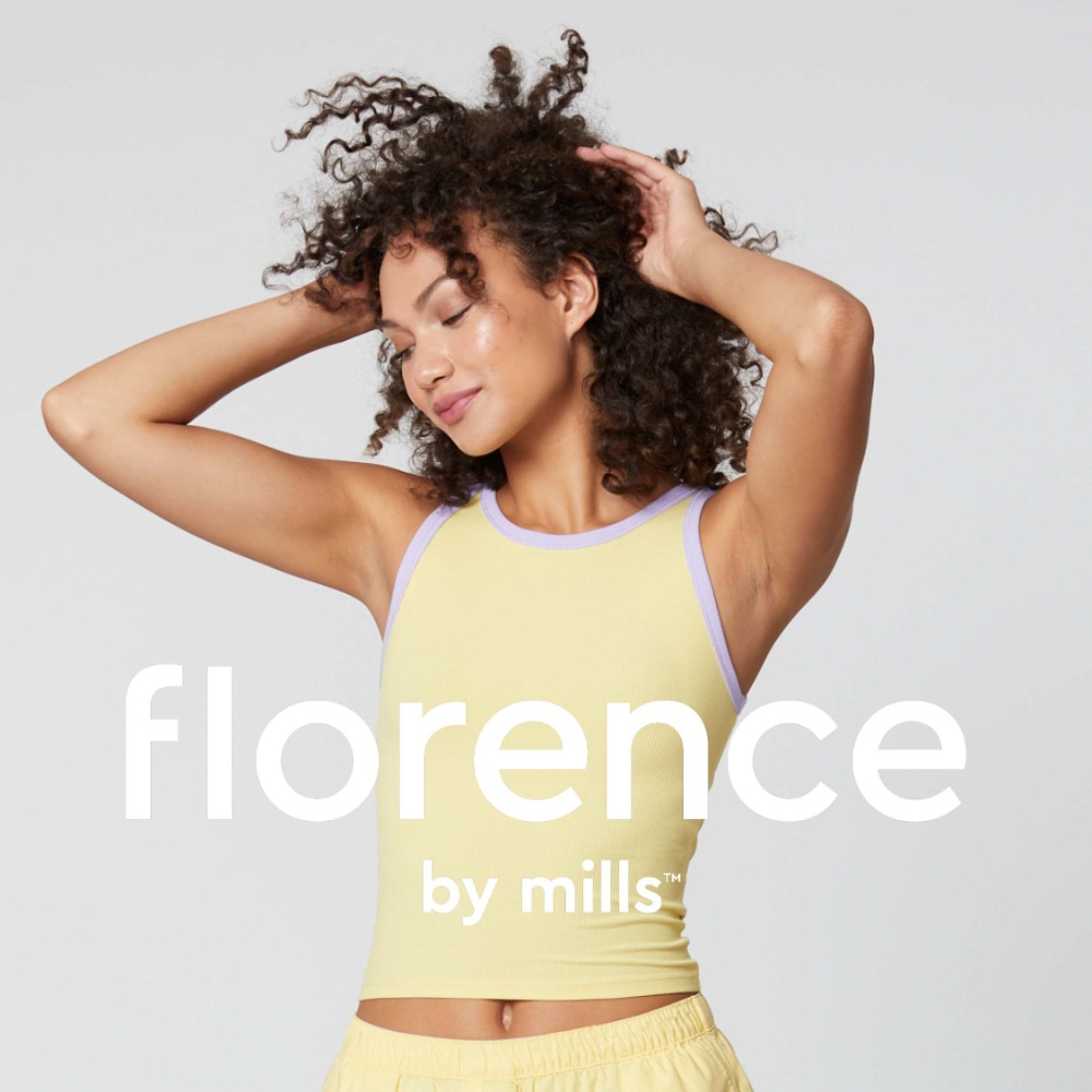 Woman with curly hair wearing a yellow tank top with lilac trim against a neutral studio background