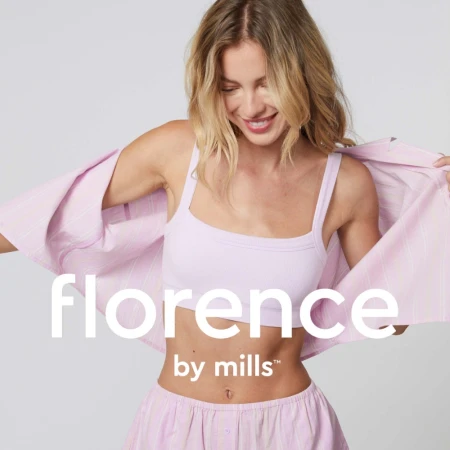 Blonde woman wearing a pink crop top and matching shorts while holding open a striped shirt against a plain background