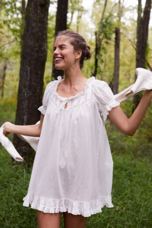 Smiling woman wearing a white ruffled dress holding out sleeves in a forest