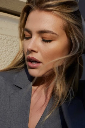 Close-up portrait of a woman with blonde hair wearing a grey blazer, photographed by Caitlin Mitchell in natural sunlight.