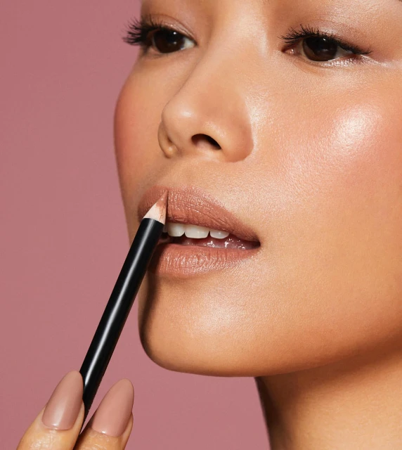 Close-up of an adult woman applying lip liner, focusing on makeup application, cosmetic pencil, and beauty routine against a solid backdrop.