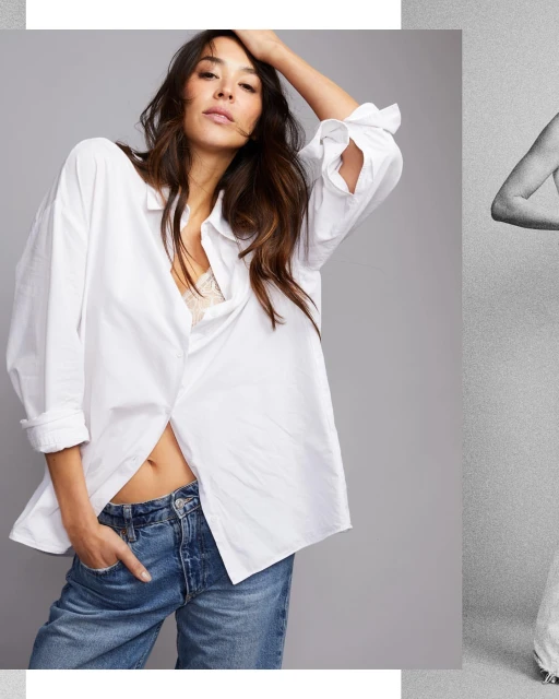 A brunette woman poses in a photo studio. She wears a white, oversized shirt and blue jeans, and looks directly at the camera.
