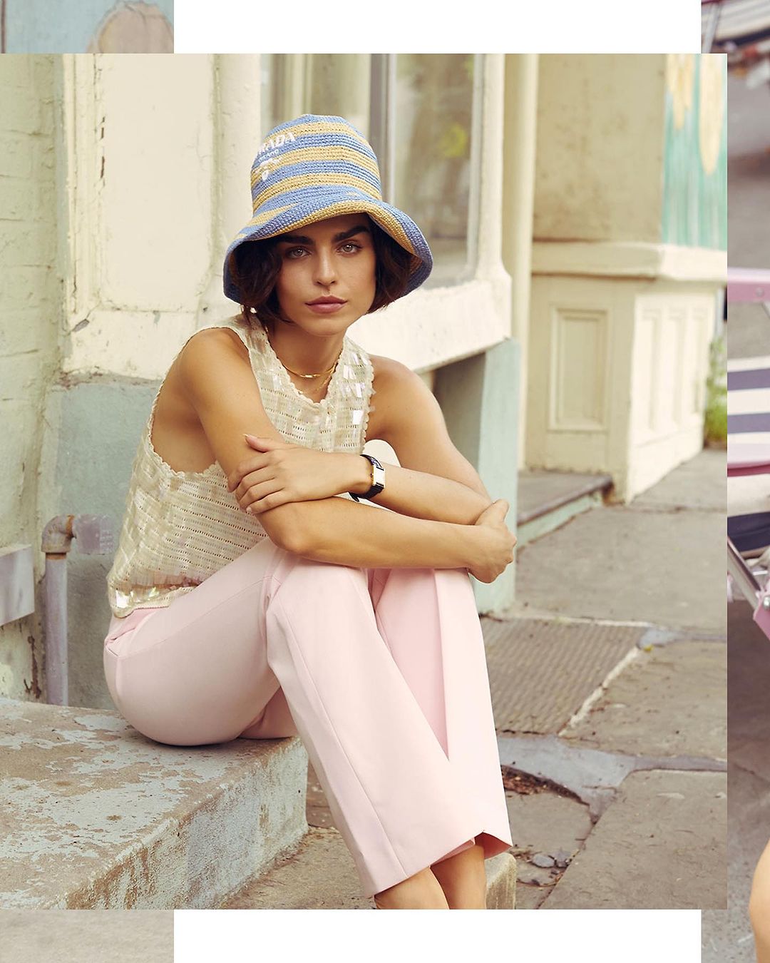 A woman in a bucket hat and sequined tank top sits on outdoor steps, styled in a pastel color palette with natural light and a building backdrop.