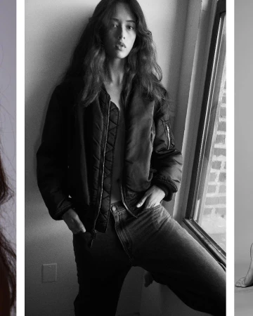 Black and white portrait of a woman leaning against a wall wearing a dark bomber jacket and jeans