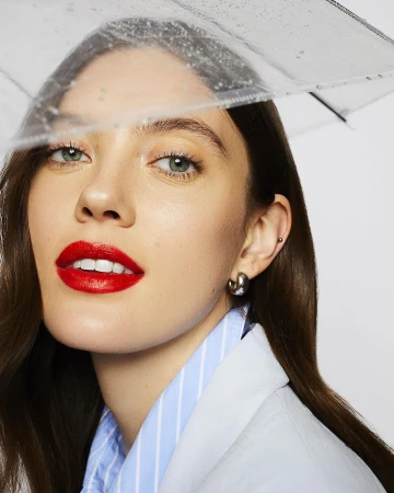 Close-up portrait of a woman wearing red lipstick and a clear umbrella, photographed by Caitlin Mitchell.