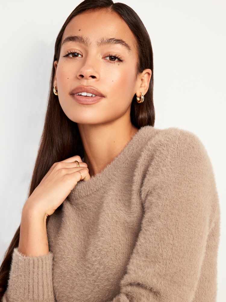 Portrait of a young woman wearing a fluffy taupe knit sweater and gold hoop earrings against a white background
