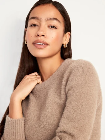 Portrait of a young woman wearing a fluffy taupe knit sweater and gold hoop earrings against a white background