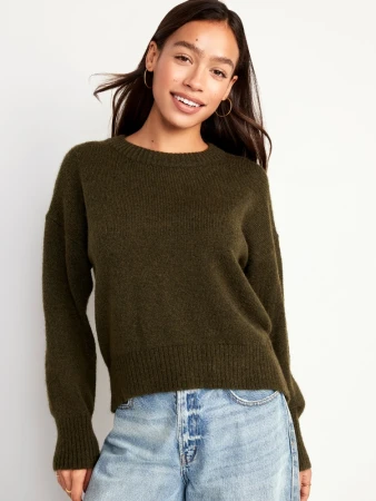 Smiling woman wearing an olive green crewneck sweater and blue jeans against a neutral background