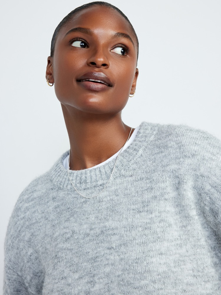 Dark-skinned woman wearing a gray sweater with a crew neck, looking up and to the right. Indoor setting and neutral background.
