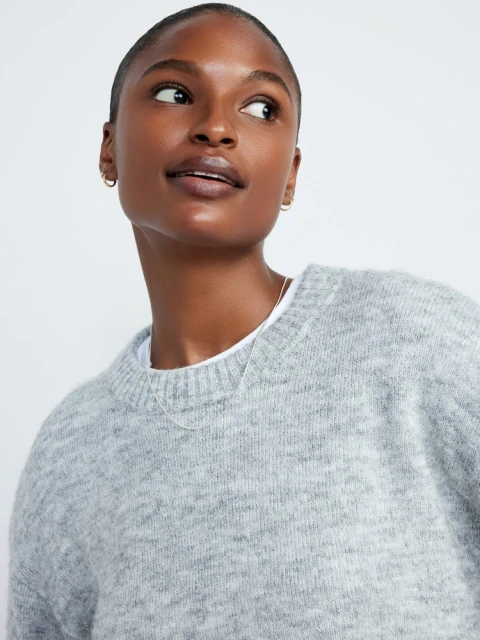 Dark-skinned woman wearing a gray sweater with a crew neck, looking up and to the right. Indoor setting and neutral background.