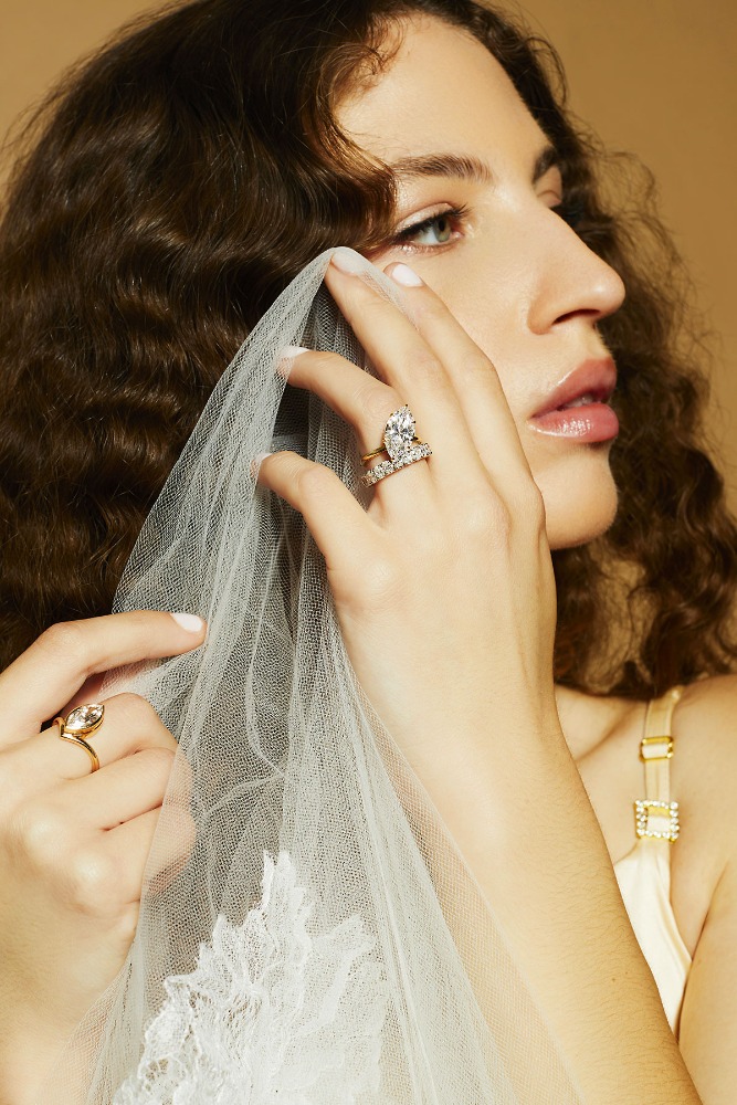 Close-up portrait of a woman wearing diamond rings holding a white lace veil by photographer Caitlin Mitchell