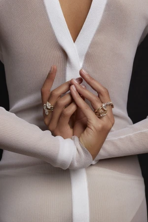 Close-up of a woman's hands adorned with intricate gold rings, set against a dark background, highlighting detail and texture.