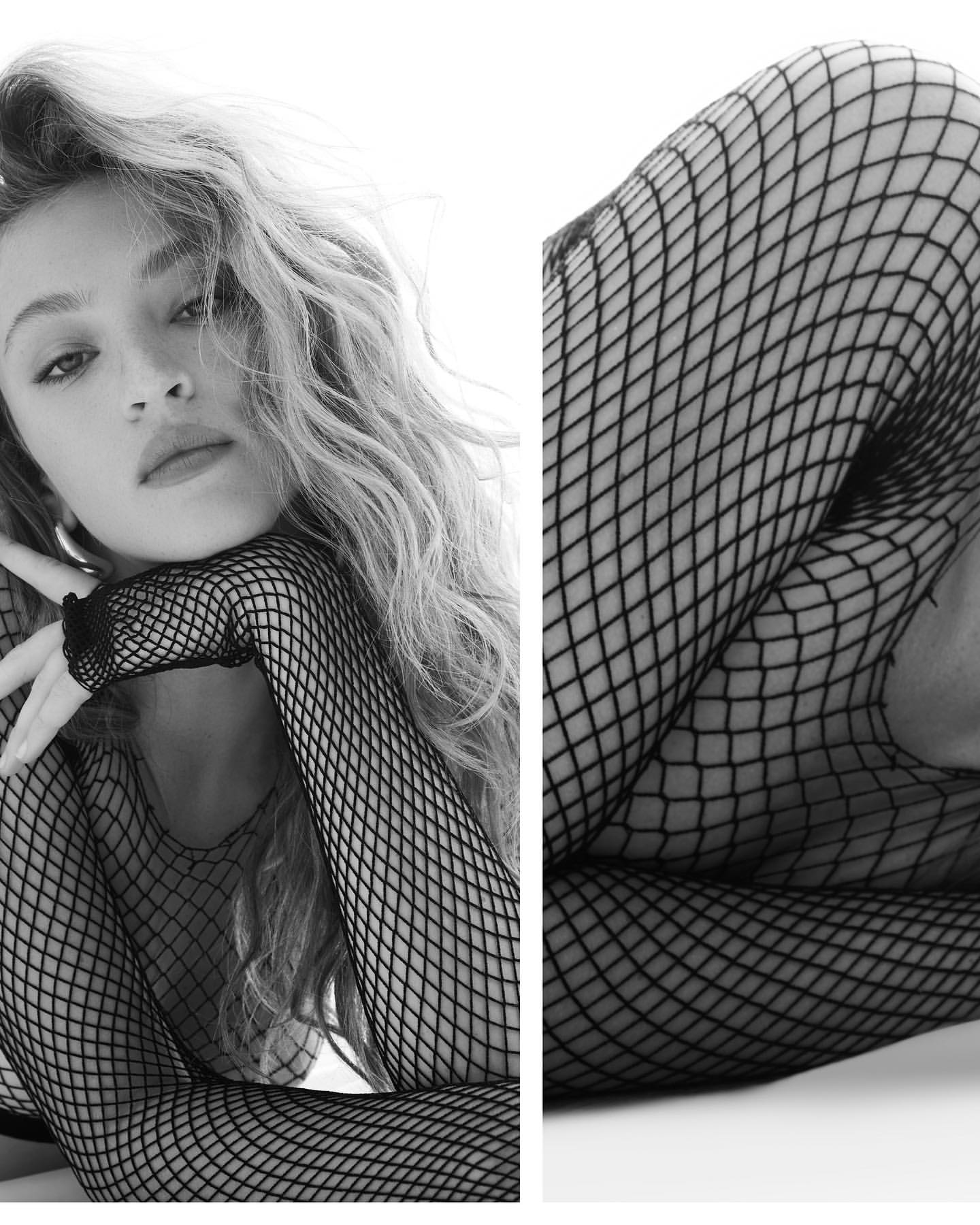 Monochrome portrait of a blonde woman wearing fishnet sleeves with her head resting on her hand, facing forward with a gentle gaze.