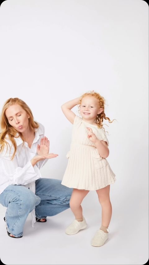 Woman in white shirt and jeans posing beside a young red-haired child against a plain white background