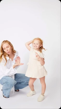 Woman in white shirt and jeans posing beside a young red-haired child against a plain white background