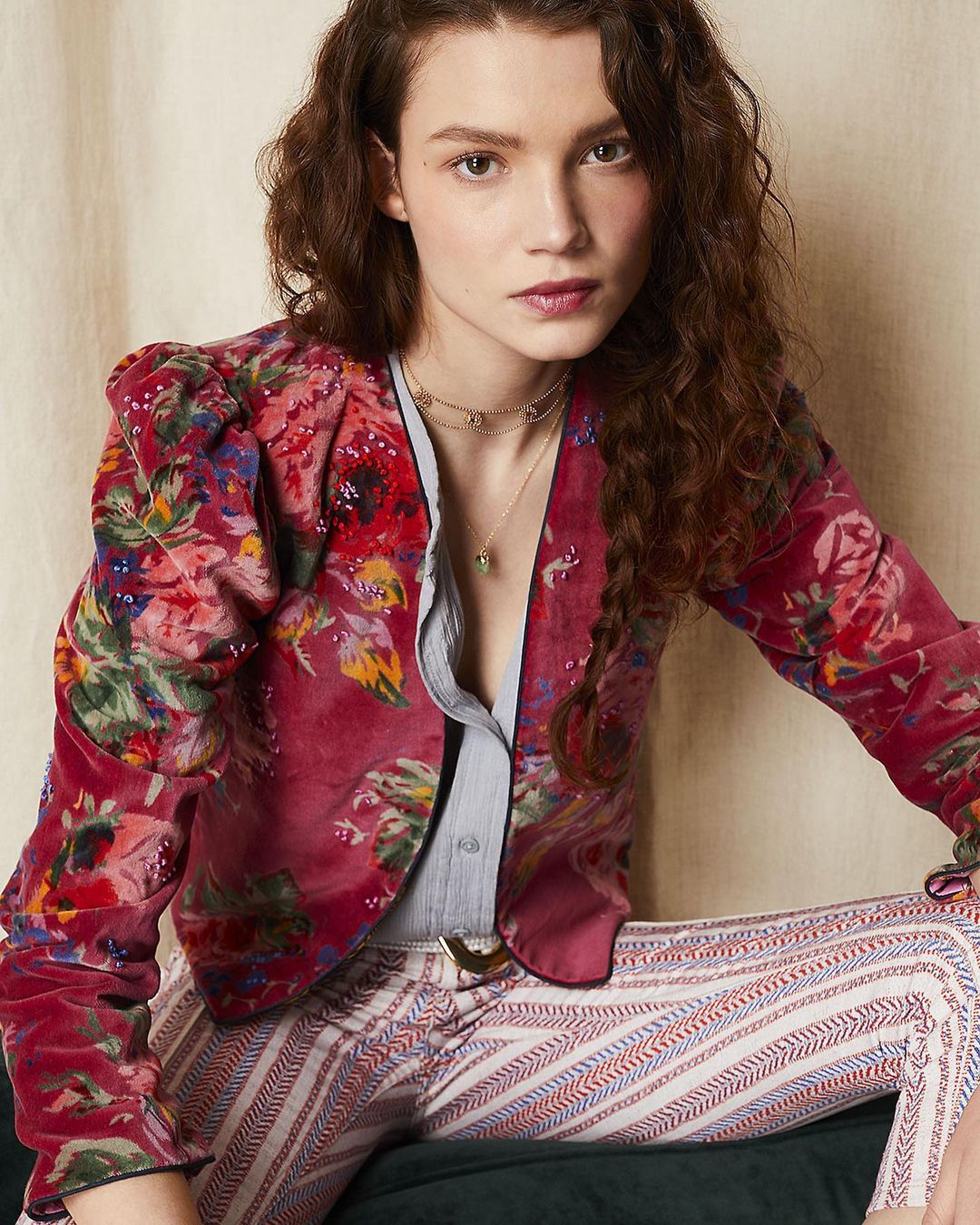 Portrait of a woman wearing a floral print jacket and striped pants, posing indoors against a neutral backdrop in a fashion setting.