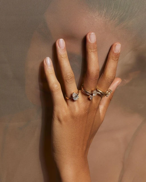 Close-up shot of a hand adorned with a set of gold rings, each featuring a unique gem, set against a warm, textured background.