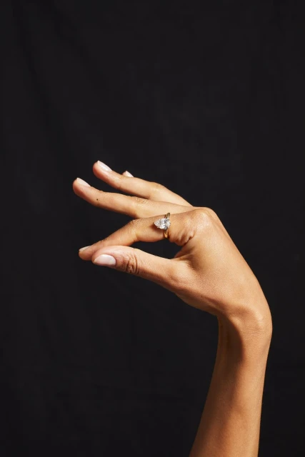 Close-up of a hand with a diamond ring. Focus on jewelry, against a solid black backdrop, emphasizing the ring's design and sparkle.