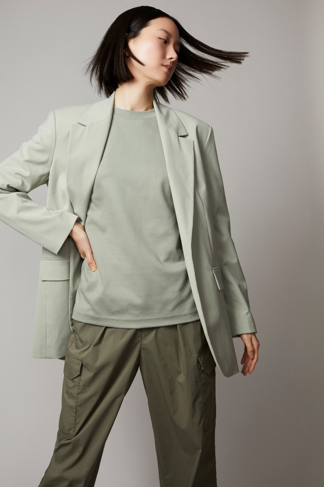 An Asian woman with shoulder-length black hair poses in a studio wearing a light-green blazer, matching t-shirt, and cargo pants.