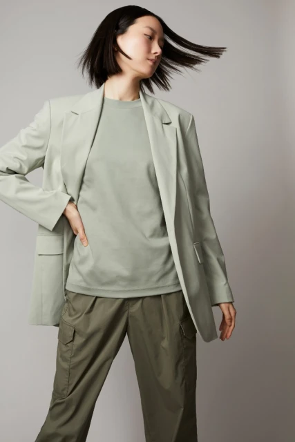 An Asian woman with shoulder-length black hair poses in a studio wearing a light-green blazer, matching t-shirt, and cargo pants.