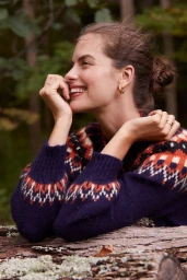 Smiling woman in navy fair isle sweater resting chin on hand outdoors with a forest background
