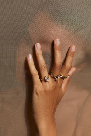 Close-up of a person's hand wearing gold diamond rings against a sheer translucent fabric covering their face