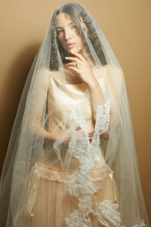 Woman wearing a sheer veil over her head, ivory satin dress, and lace trim, photographed by Caitlin Mitchell
