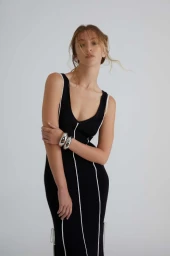 Woman in a black dress with white piping wearing silver bangles against a grey seamless background