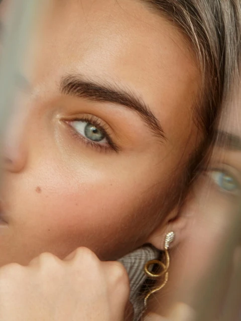 A fair-skinned adult female model poses in a photo studio wearing a black turtleneck and blue jeans in a close-up, eye-level studio shot.