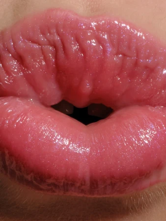 Extreme close-up of glossy pink lips pursed together in a pout, revealing a tiny gap between teeth
