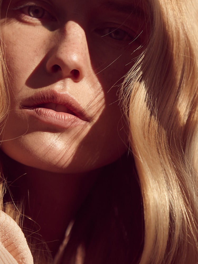 Close-up portrait of a woman with blonde hair and freckles under warm sunlight by Louise Samuelsen.