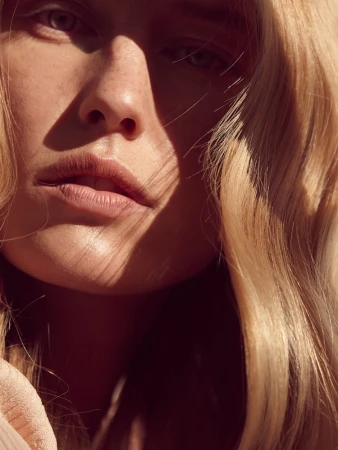 Close-up portrait of a woman with blonde hair and freckles under warm sunlight by Louise Samuelsen.