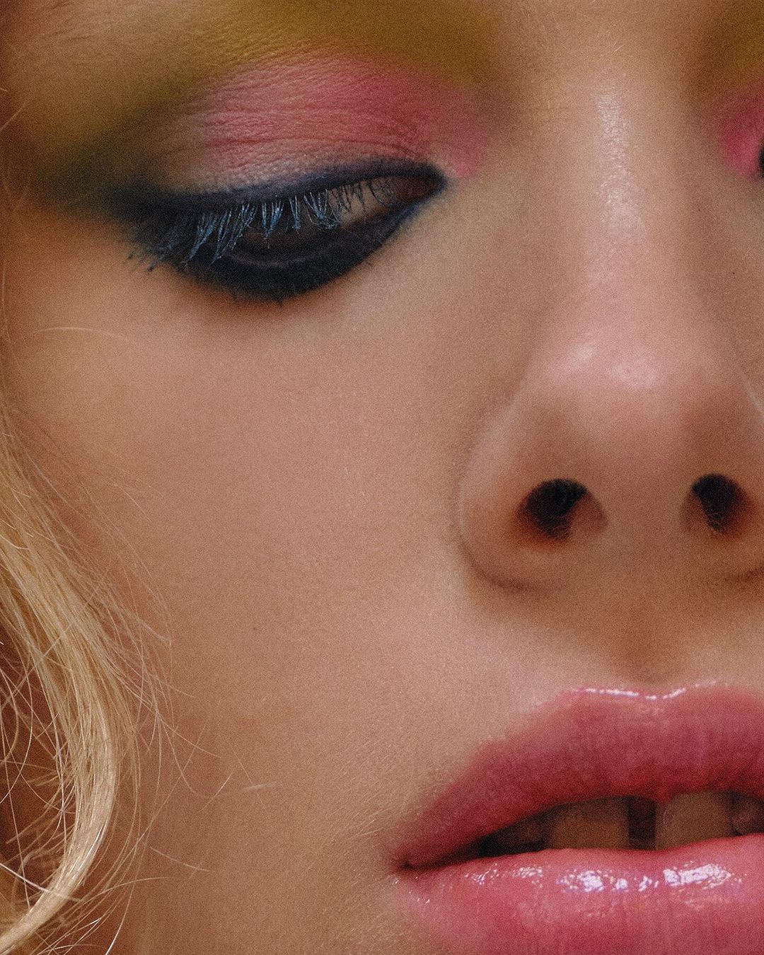 Close-up portrait of a woman with colorful eye makeup, pink eyeshadow, and glossy lips photographed by Louise Samuelsen.
