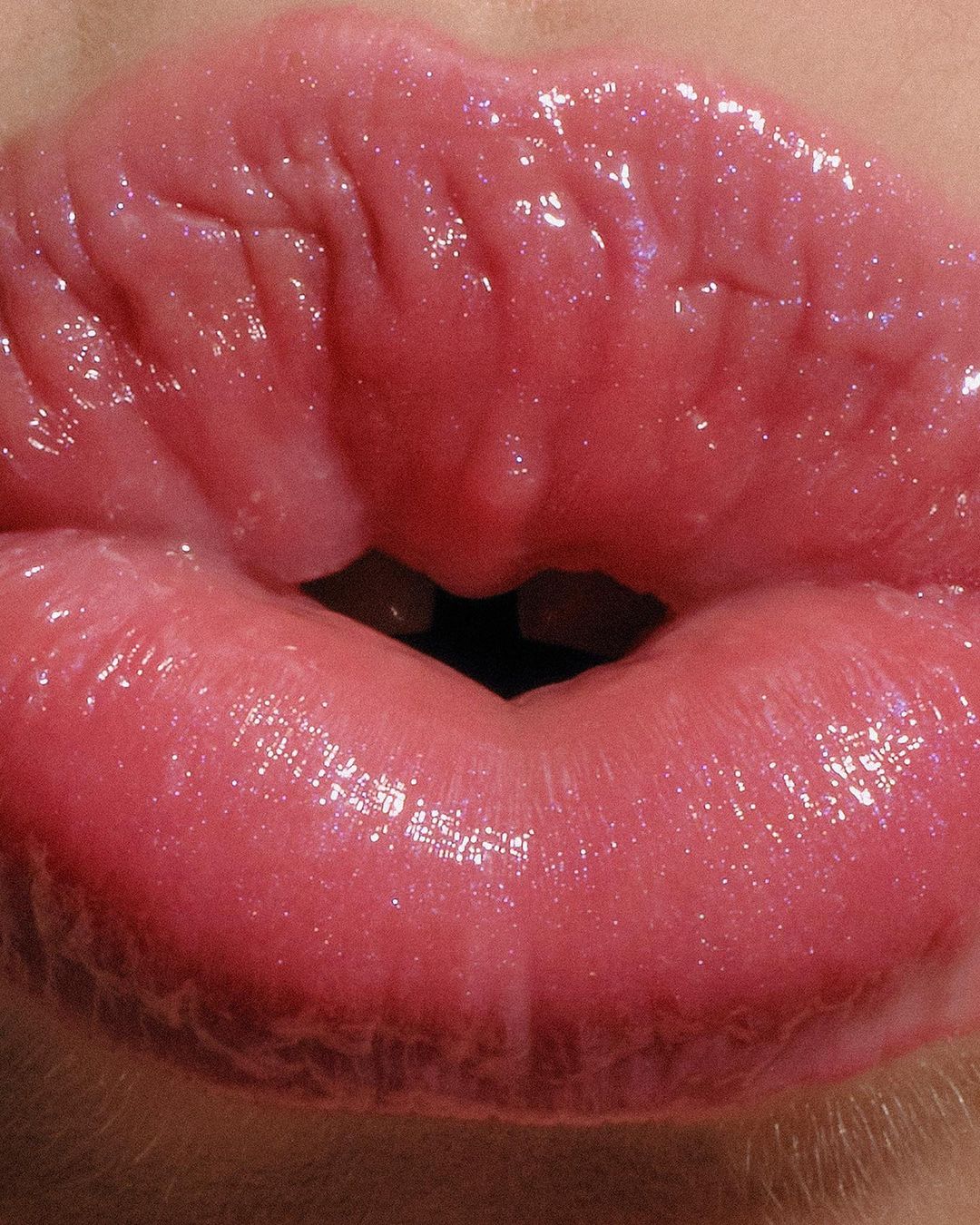 Close-up shot of glossy pink lips with visible texture and light reflection, showcasing beauty and makeup trends.