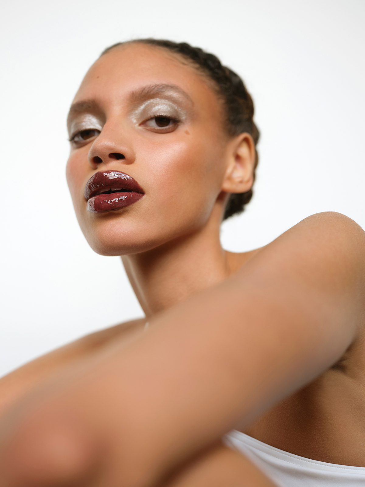Close-up portrait of an adult woman with a glossy dark lip and silvery eye shadow against a bright white background.