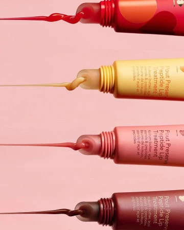 Close-up studio shot of colorful lip treatment tubes with product extruding, against a light pink background, creating a vibrant beauty aesthetic.