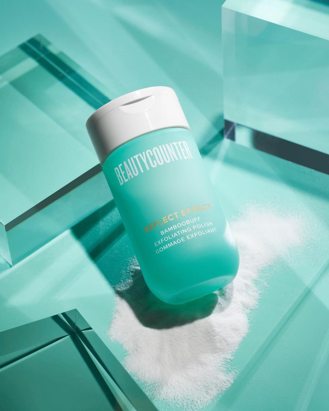 Beautycounter exfoliating polish product shot on a teal surface with geometric shapes and white powder.