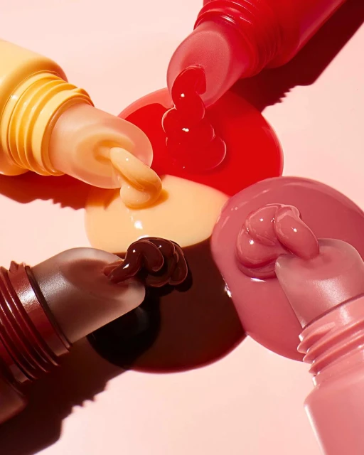 Close-up of colorful cosmetic products including tubes with applicators and a swirl of product in shades of pink, brown, red, and yellow.