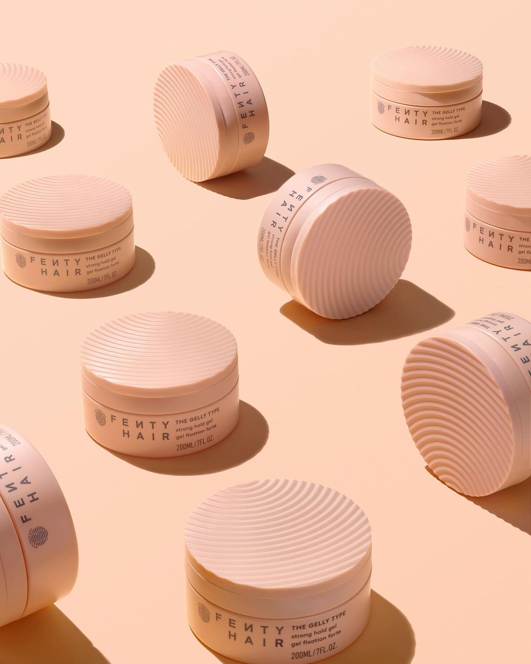 Multiple pink Fenty Hair gel products arranged on a light peach background in studio lighting, beauty shot for product marketing.