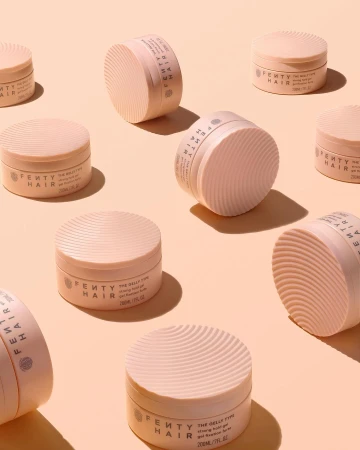 Multiple pink Fenty Hair gel products arranged on a light peach background in studio lighting, beauty shot for product marketing.
