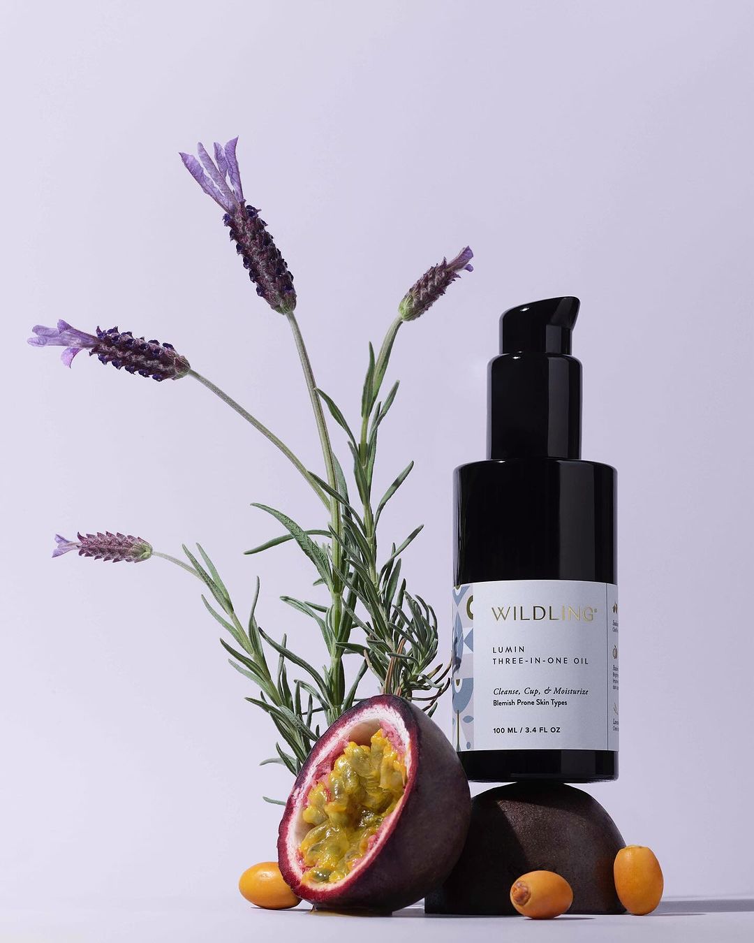 Product shot of Wildlight Lemon Three-In-One Oil with lavender, passion fruit, and kumquats on a gradient white to light purple background.