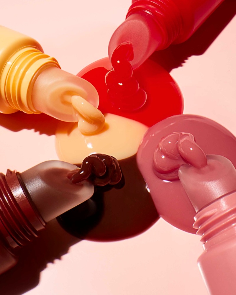 Close-up shot of colorful creams or beauty products squeezing out of their tubes against a pastel pink backdrop.