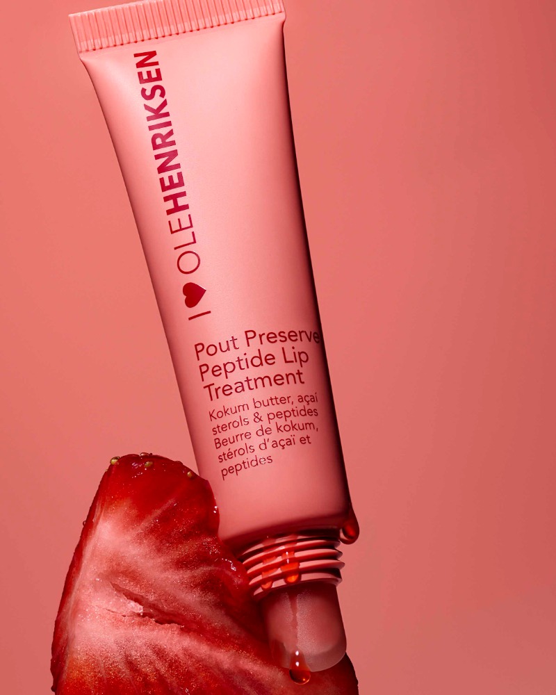 Ole Henriksen lip treatment tube with a strawberry on a peach-colored background, skincare product and fruit still life.