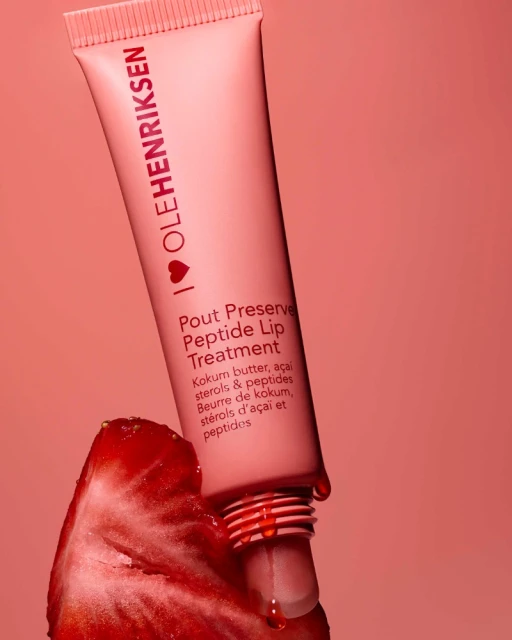 Ole Henriksen lip treatment tube with a strawberry on a peach-colored background, skincare product and fruit still life.