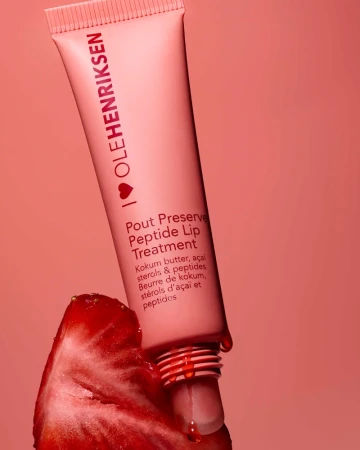 Ole Henriksen lip treatment tube with a strawberry on a peach-colored background, skincare product and fruit still life.